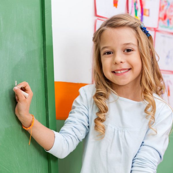 Portrait of cute little girl writing on board in kindergarten